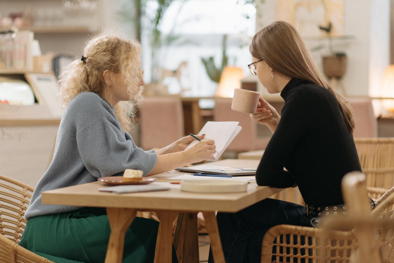 Two women in a focused one-on-one conversation at a cafe, representing personalized dating coaching support